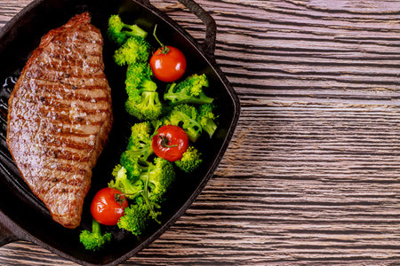 Grilled rare beef steak with broccoli and tomato on grill pan on wooden background.の写真素材