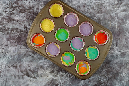 Twelve pieces of color raw cupcakes on oven tray.