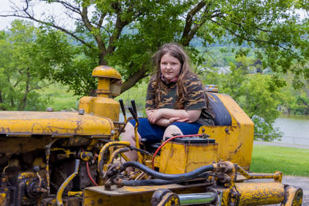 Young girl sitting on old yellow tractor in countryside.の写真素材