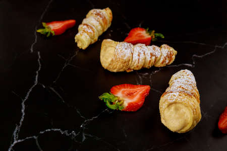 Crispy sweet rolls with whipped cream and strawberries on black background.の写真素材