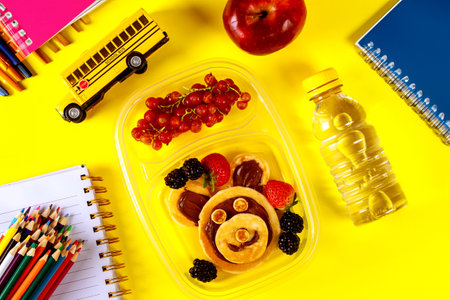 Lunch box with fanny face pancakes fruits and water for school.の写真素材
