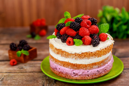 Delicious, multi layered cake features raspberry and blackberry fillings, topped with fresh berries and mint leaves, presented on vibrant green plate.の写真素材
