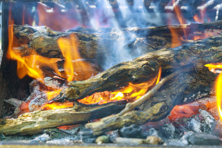 Warm flames dance among burning wood, casting glow and producing gentle smoke. Fire crackles softly, creating cozy atmosphere perfect for outdoor activities with friends.の写真素材