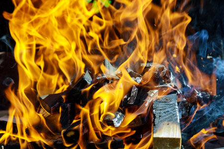 Bright, dancing flames rise from pile of firewood, illuminating surrounding area during lively summer evening gathering. Warm glow enhances atmosphere as friends enjoy outdoors.の写真素材