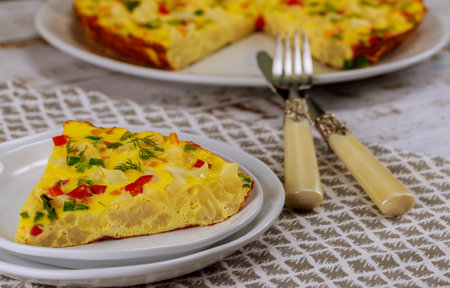 Slice of vegetable frittata served on white plate, showcasing its vibrant colors from peppers and herbs. Dish perfect for breakfast or brunch gatherings.の写真素材