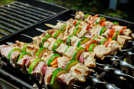 Skewers of marinated chicken, bell peppers, and onions grilling over outdoor barbecue in backyard during sunny summer day. Aroma fills air, inviting everyone.の写真素材