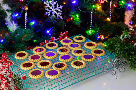 Festive cookies adorn cooling rack, showcasing vibrant colors and glazes. Warm, cheerful atmosphere radiates from decorated Christmas tree in background.の写真素材