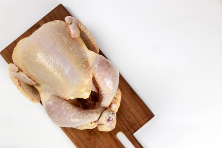 Whole chicken placed on wooden cutting board, showcasing its pale skin and raw form. Setting well-lit, indicating clean kitchen atmosphere suitable for cooking.の写真素材