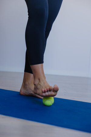barefoot feet rolling green ball on blue mat, self myofascial release focused on plantar and ankle mobility;の写真素材