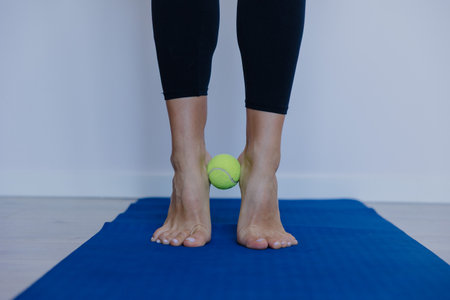 Close-up of feet, Woman doing foot gymnastics with tennis ball on yoga mat, close-up planの写真素材