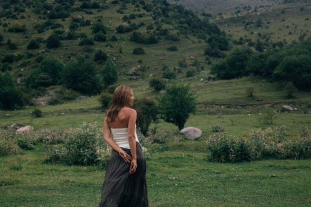 woman standing at valley lookout, contemplative pose with hands behind back, panoramic green views,の写真素材