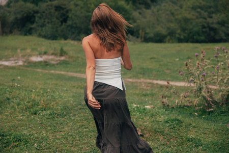 back view caucasian woman walking through valley, exploratory mood with flowing skirt, distant hills,の写真素材