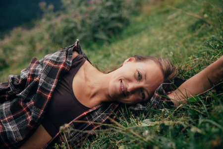 white woman reclining in grass smiling, relaxed meadow scene, playful gaze, flannel shirt, mood of freedomの写真素材