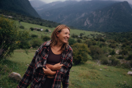 pregnant caucasian woman outdoors smiling, in plaid shirt and brown top, standing in alpine valley, handsの写真素材