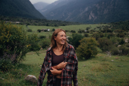 caucasian woman traveler mountain valley, wearing plaid shirt over brown top, hands clasped near waist,の写真素材