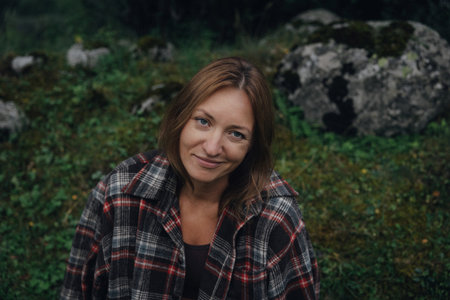 white woman sitting on mossy rock smiling gently, flannel shirt and pastoral backdrop, quiet homestead energy,の写真素材