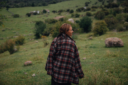 white woman walking away across meadow in flannel, back turned to camera, contemplative slow journeyの写真素材