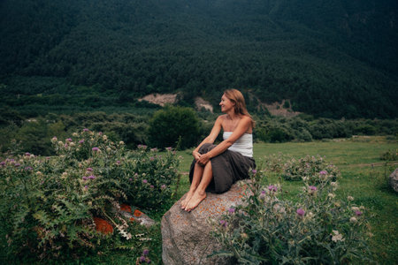 contemplative caucasian woman sitting on rock, reflective mountain retreat with wildflowers, calm posture,の写真素材