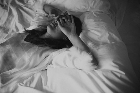 woman lying in bed, morning light, writer exhausted, rumpled sheets, hand over forehead, monochrome filmgrain,の写真素材
