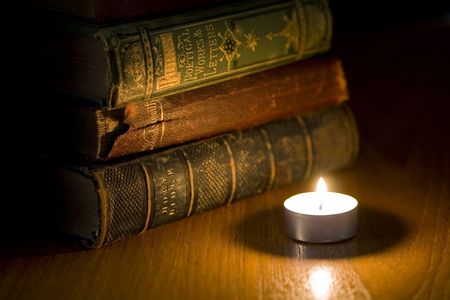 a pile of old books next to a small candleの写真素材