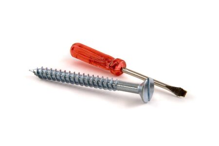 An isolated picture of a very small, red-handled screwdriver lying next to a large screw.の写真素材