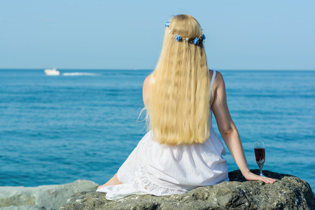 girl seating on coastline with glass of wineの写真素材