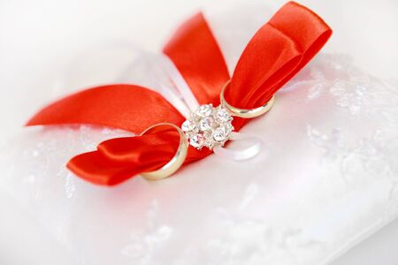 Gold wedding rings on a satiny pillow with red tapesの写真素材