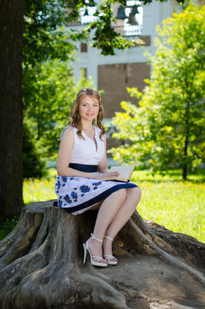 A girl with a book sitting near a treeの写真素材