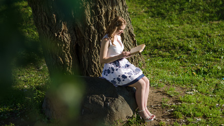 A girl with a book sitting near a treeの写真素材