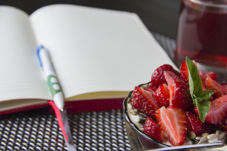 Porridge with strawberries and open notebook to plan daily business during breakfastの写真素材