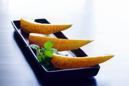 Three slices of melon on a black rectangular plate with lemon balm leaf, minimalist styleの写真素材
