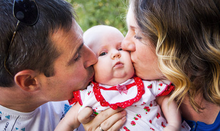 Parents kissing baby. Mom and Dad kissing baby on the cheek - the image of a happy family.