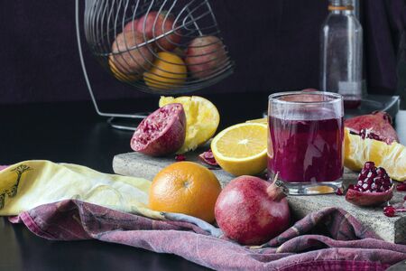 Freshly squeezed with the help of a mechanical press, the juice of pomegranate and orange. Juicy fresh pieces of fruit on a wooden surface. Dark background, daylight.の写真素材