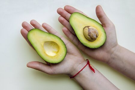 Two halves of fresh ripe avocado on children's palmsの写真素材