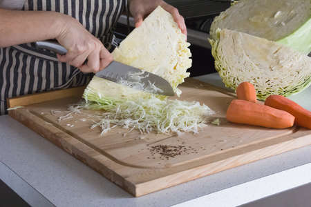 three bright carrots and a huge cut head of juicy cabbage on a cutting board, a woman is cutting cabbage with a large kitchen knifeの写真素材