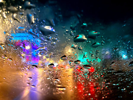 Raindrops and wet snow on the car window against the background of the city and cars, multicolored...