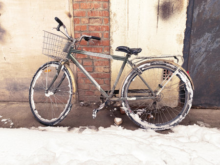 Old bike near old brick wall on winter snowy streetの写真素材