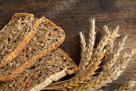 Three slices of whole grain bread next to spikelets of wheat on a dark cutting board. Flat lay.の写真素材