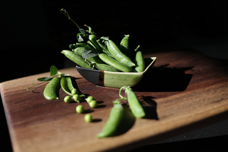 Delicious ripe green peas lie in a small ceramic bowl and on a wooden table. Dark background, rustic...