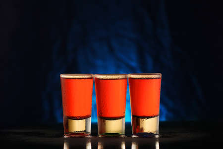 three glasses with red alcohol on a black background with a blue gradientの写真素材