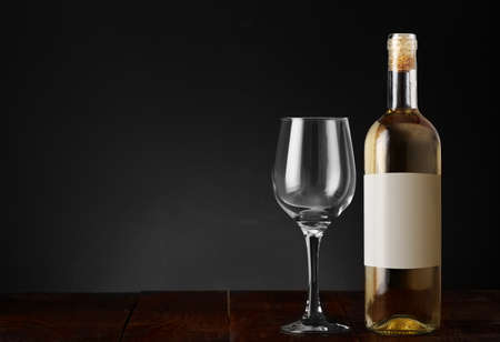 wine bottle with empty goblet on wooden table and black backgroundの写真素材