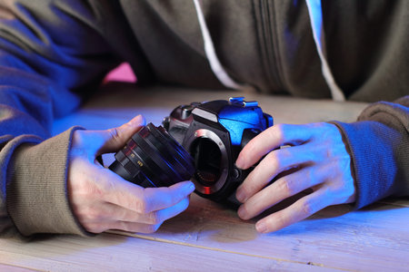 Removing an old lens from a SLR camera by a person in a green sweatshirtの写真素材