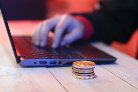 a pile of coins on a table next to a laptop and a person's hand on a colored background