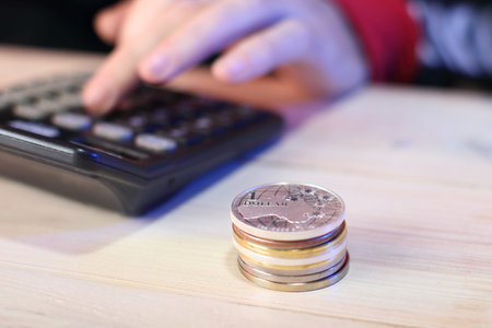 a pile of coins next to a calculator with a hand on the table
