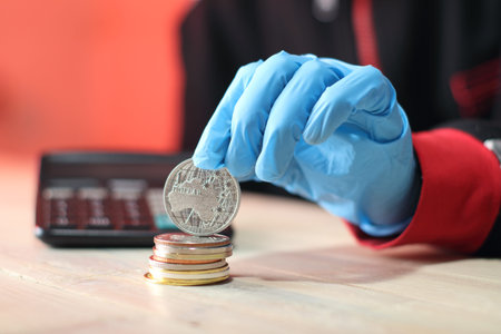 a silver australian coin held on a pile of coins by a person wearing blue gloves against a colored...