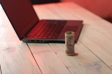 a roll of Polish banknotes next to a laptop on a table and a colored background