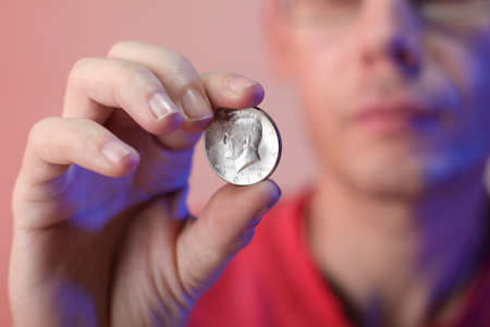a person holding a coin in his right hand on a colored backgroundの写真素材