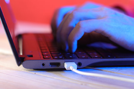 white usb cable in laptop port with hands on keyboard and colored background