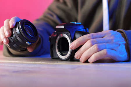 a person holding an old SLR camera with an old lens on a table and a colored background