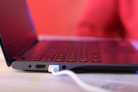 old laptop with usb cable on table and pink background
